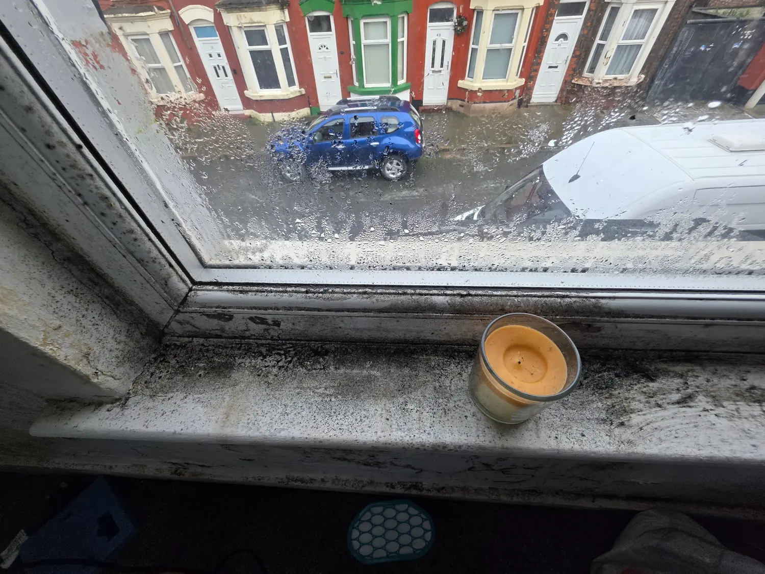 A window sill and frame blackened with mould, with condensation still running down the glass above it