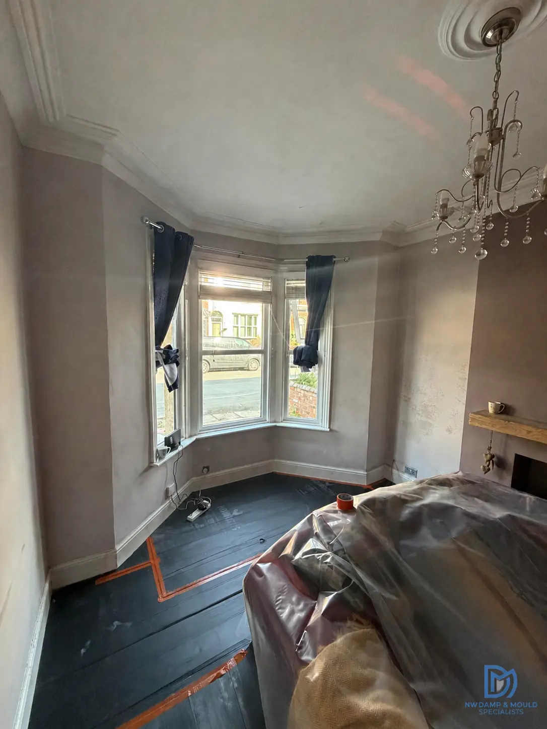 A Southport bay window room before any work starts, its walls stained and blown with damp and the furniture already sheeted up.