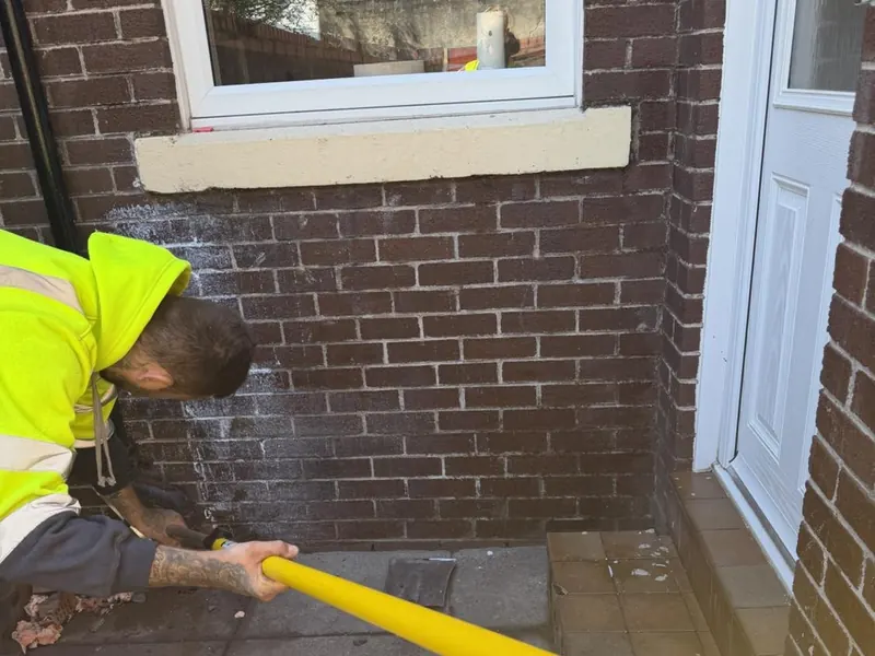 An operative applying a breathable water repellent to a repointed brick elevation
