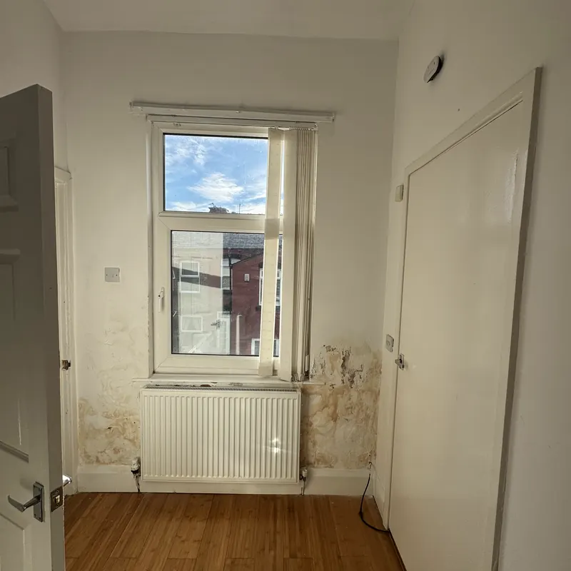 A cold back room with damp patches spreading across the wall either side of the window