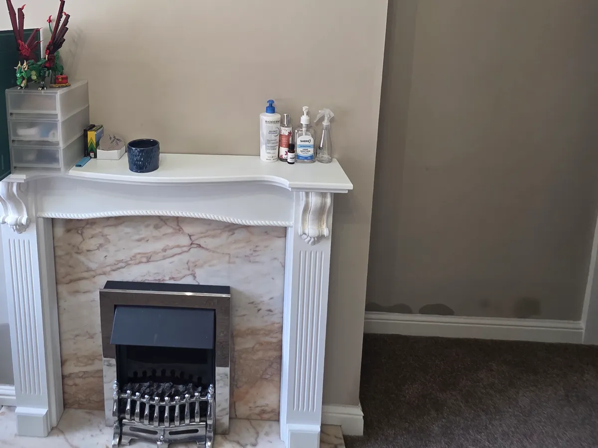 Damp staining along the base of a living room wall, just above the skirting board, beside a fireplace.
